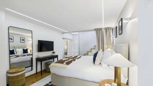 Une chambre d’hôtel moderne dotée d’un grand lit, d’une télévision à écran plat, d’une table de chevet avec une lampe et d’un grand miroir.