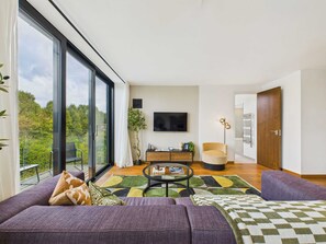 Un salon moderne avec une grande fenêtre, un canapé, une table basse et un téléviseur.