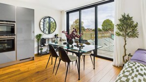 Une cuisine moderne dotée d’appareils électroménagers intégrés, un coin repas avec une table et des chaises en verre, et une grande fenêtre offrant une vue sur la ville.