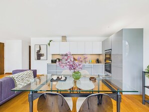 Una sala moderna con una mesa de vidrio, un sofá púrpura y una cocina al fondo.