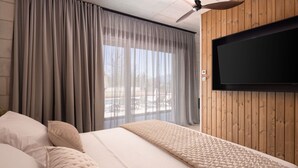 Ein Hotelzimmer mit Bett, Vorhängen, einem an einer Holzwand montierten Fernseher und einem Deckenventilator.
