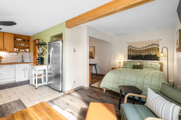 A compact living space with a kitchenette, a bed with green bedding, and a dining area.