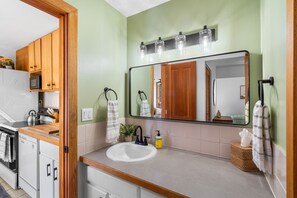 A modern kitchen with a white sink, wooden cabinets, and a large mirror with three light fixtures above it.
