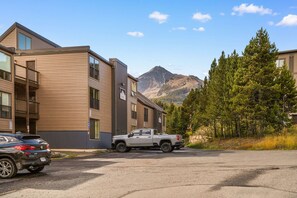 A multi-story building with a parking area, a pickup truck, and a mountainous backdrop.