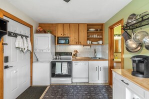 A compact kitchen with white appliances, wooden cabinets, and a black patterned rug.