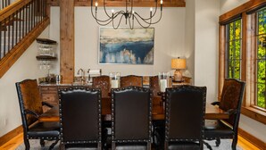 A dining area with a wooden table and chairs, a chandelier, and a painting of a cityscape. - Ski-In/Ski-Out Luxury | Cowboy Heaven Retreat (Big Sky)