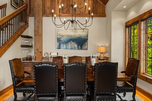 A dining area with a wooden table and chairs, a chandelier, and a painting of a cityscape.