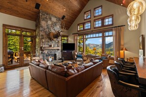 Un amplio salón con chimenea de piedra, asientos de cuero y ventanas grandes con vistas a la montaña.