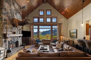 A spacious living room with a stone fireplace, leather sofa, and a large window offering a mountain view.