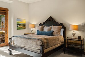 A neatly made bed with a quilt, two bedside lamps, and a painting on the wall.