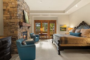 A bedroom with a stone fireplace, a bed with a headboard, a desk, and a chair.
