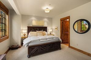 Un dormitorio con una cama grande, dos mesitas de noche con lámparas, una puerta de madera y un espejo redondo en la pared.