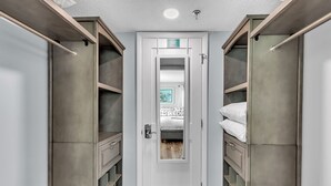 Een kamer met een centrale deur, kasten aan weerszijden en een bed met een witte matras en grijze deken.