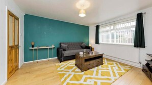 Una sala de estar con una pared de acento color turquesa, un sofá gris, una mesa de centro de madera y un tapete amarillo estampado.