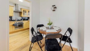 Una cocina compacta con armarios de madera y una campana extractora de acero inoxidable. Una mesa de comedor con cuatro sillas se encuentra centrada en la habitación, acompañada por una pequeña planta en maceta.