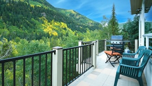 Ein Balkon mit Grill, zwei Stühlen und Blick auf einen bewaldeten Berg.