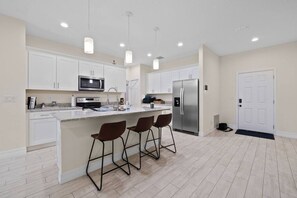 Una cocina moderna con armarios blancos, un refrigerador de acero inoxidable, un microondas y una isla grande con taburetes de bar.