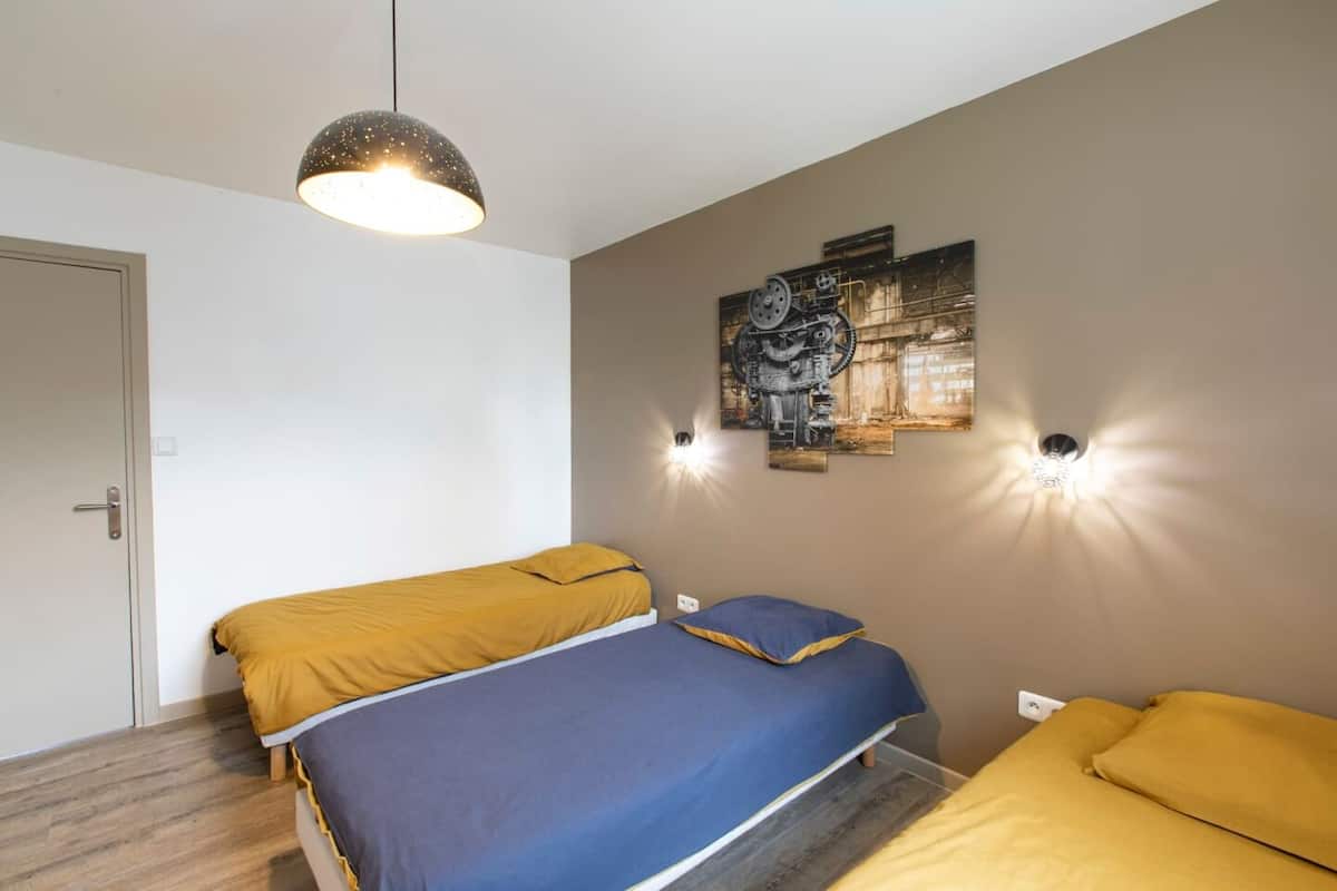 A bedroom with two beds, a ceiling light, and a wall-mounted artwork.