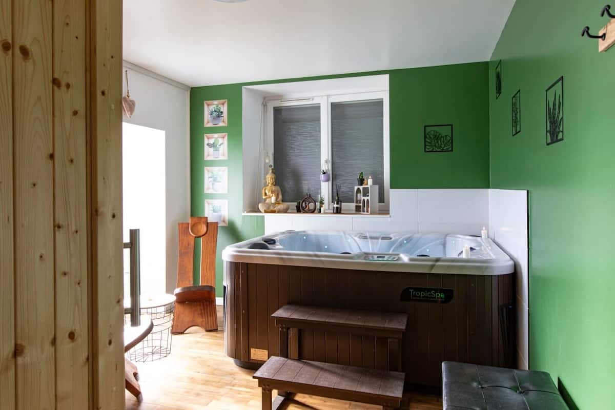 A room with a large hot tub, wooden flooring, a window, and green walls.