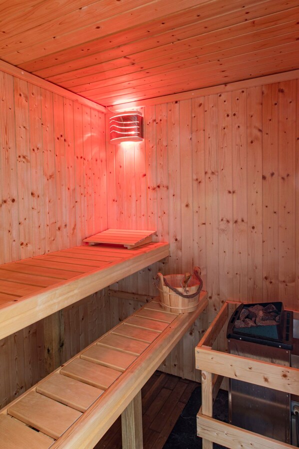 A sauna with wooden walls and benches, a heater, and a basket. - Les gîtes de la commanderie de SaintJean (Beynat)