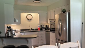 A kitchen with a central island, two bar stools, a wooden dining table, and a refrigerator. - The Cardinal House 1A. In a Stunning area, see the deer pass by! (Savannah)