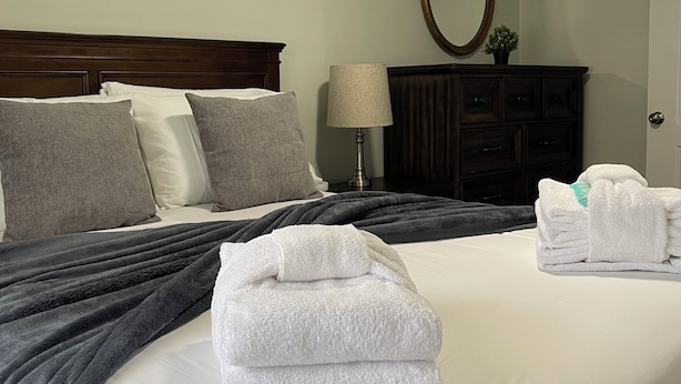 A neatly made bed with white and grey linens, a dark headboard, and a bedside lamp. - The Cardinal House 1A. In a Stunning area, see the deer pass by! (Savannah)