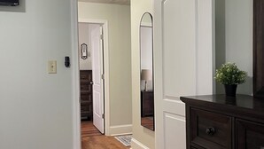 A hallway with wooden flooring, a white door, and a dark wooden dresser with a plant on top. - The Cardinal House 1A. In a Stunning area, see the deer pass by! (Savannah)