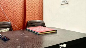 Un salón de conferencias con papel tapiz estampado, una mesa negra, dos sillas, un cuaderno y un ventilador de techo.