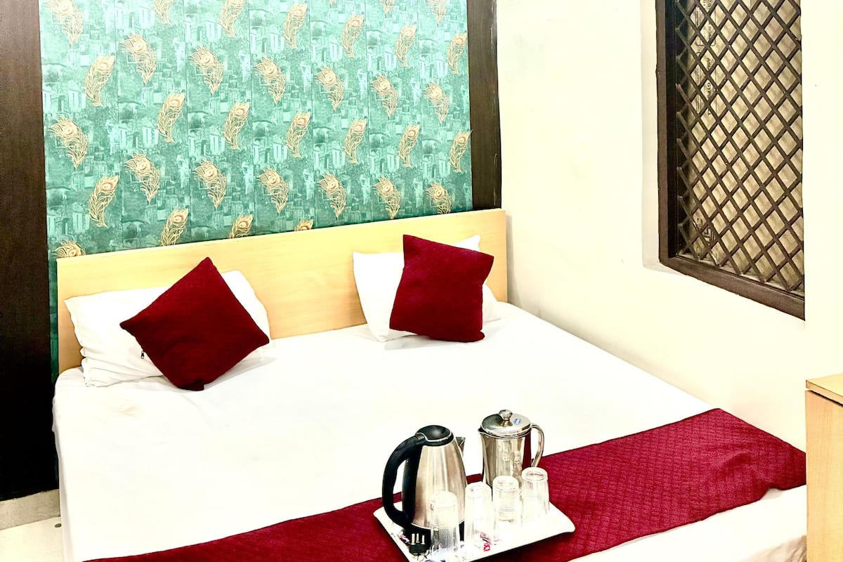 A neatly made bed with a red blanket and pillows, a tray with a kettle and cups, and a patterned wallpaper on the wall.