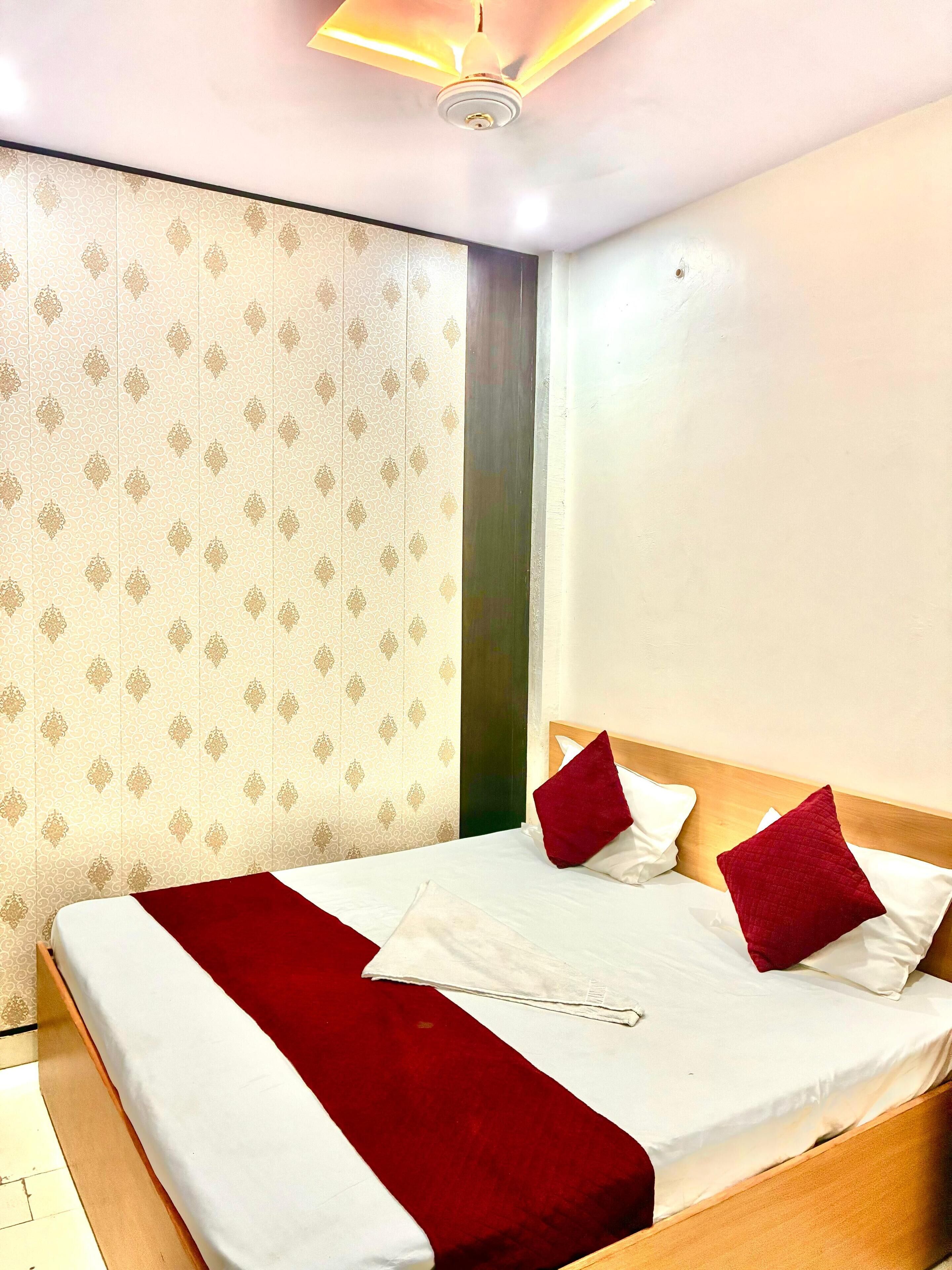 Une chambre d’hôtel avec un lit bien fait, un plaid rouge et un rideau à motifs.