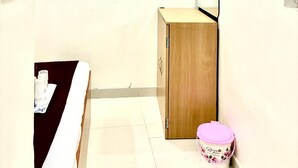 Una habitación pequeña y poco amoblada con un armario de madera, un televisor en la pared y un bote de basura rosa.