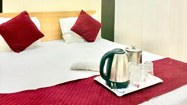 Habitación de hotel con cama, almohadas rojas, colcha roja, hervidor y bandeja con vasos y un termo.