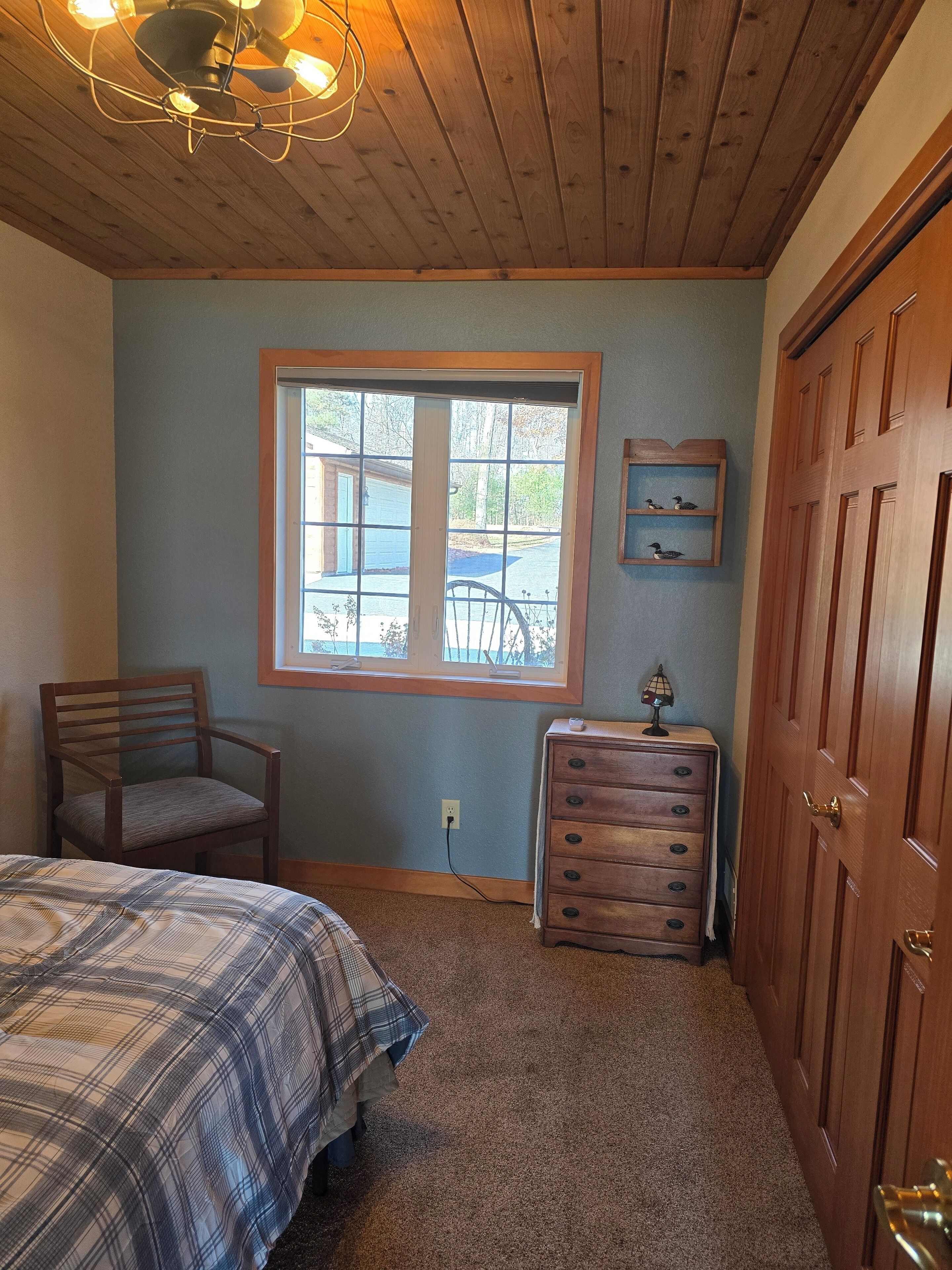 A bedroom with a bed, a chair, a dresser, a window, and a door.
