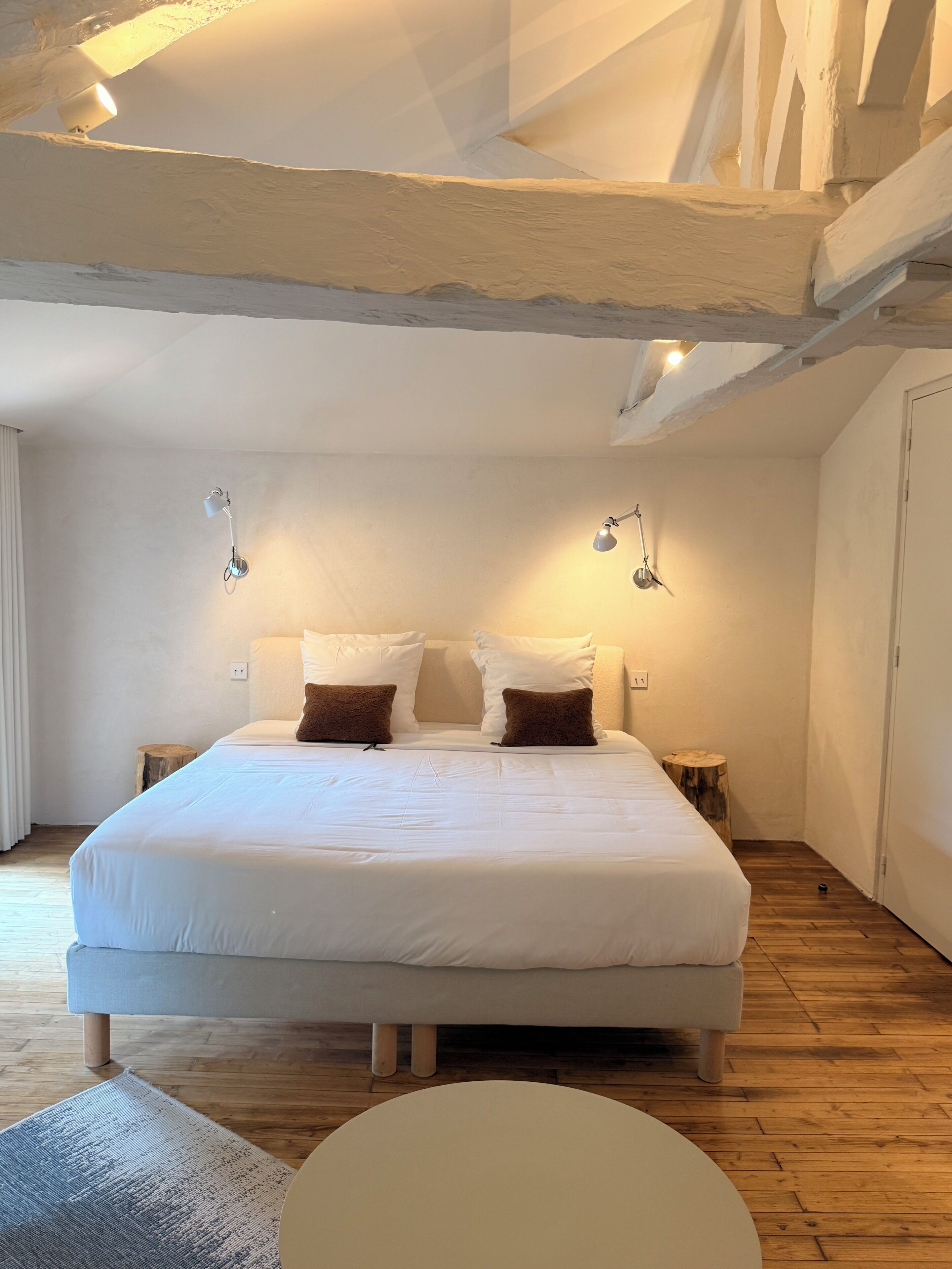 A bedroom with a large bed, two bedside lamps, a wooden floor, and a round table.