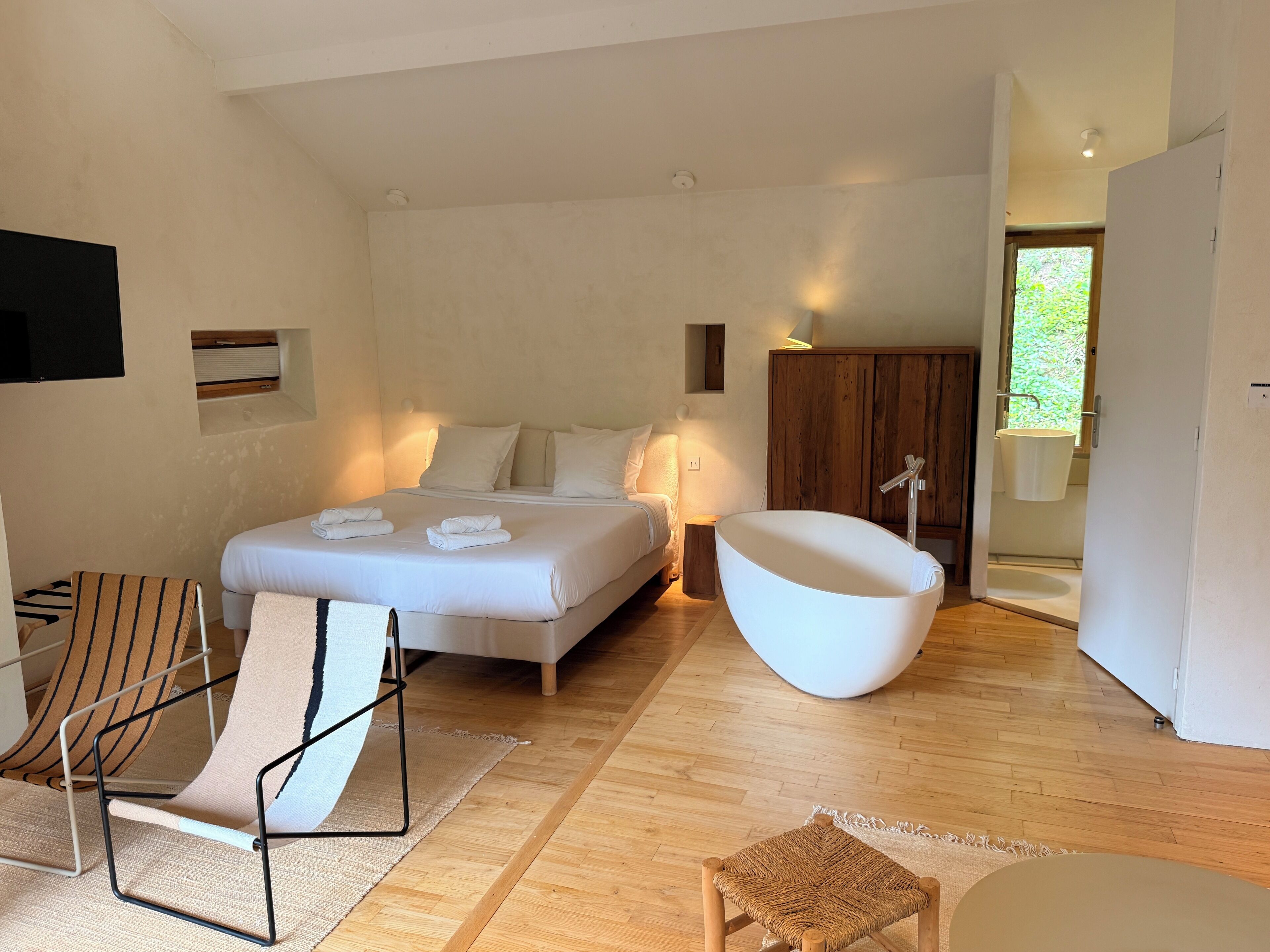 A modern bedroom with a large bed, a unique bathtub, a wooden chair, and a small table.