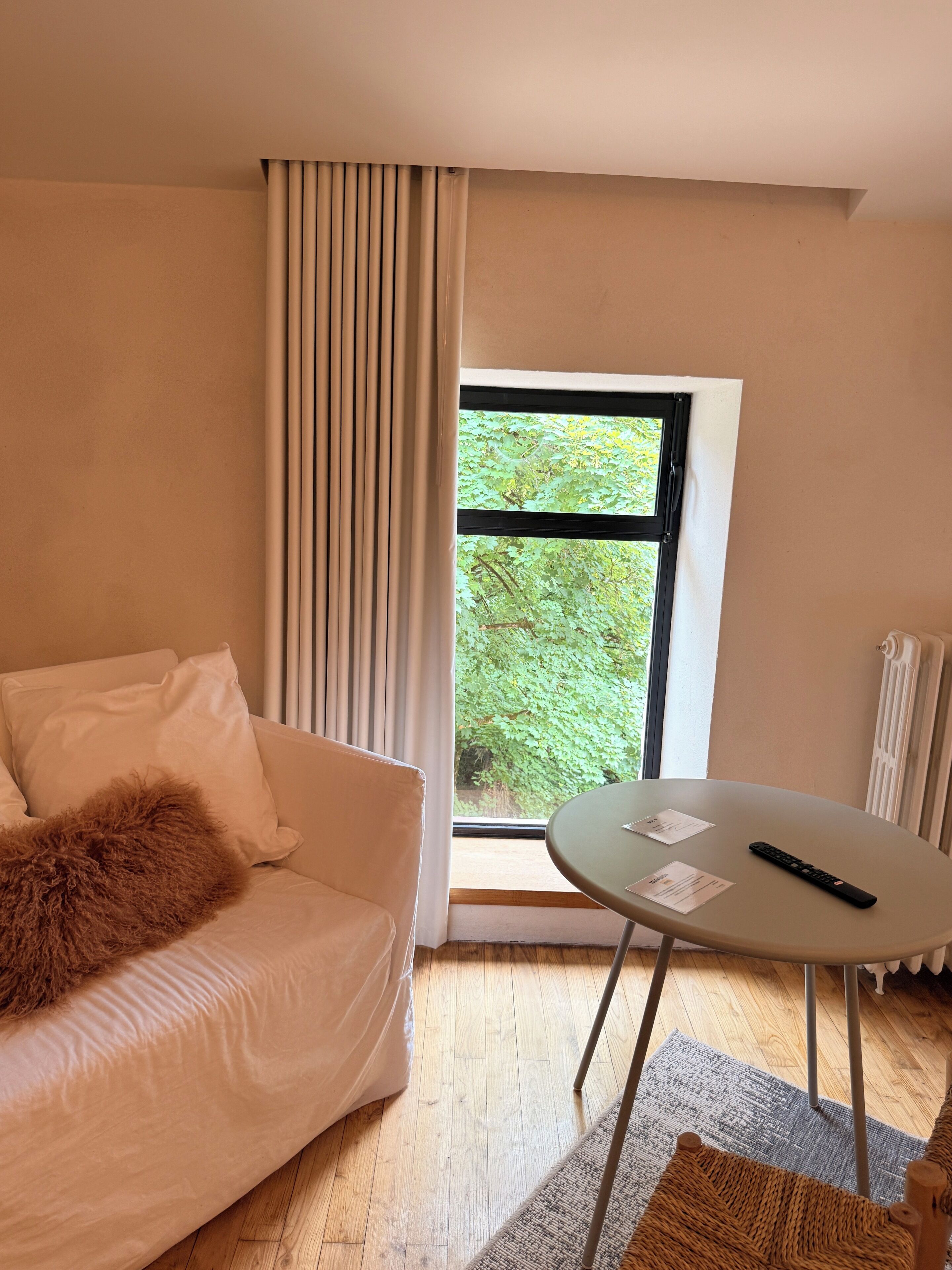 A modern room with a white sofa, a small round table, and a window with a view of greenery.