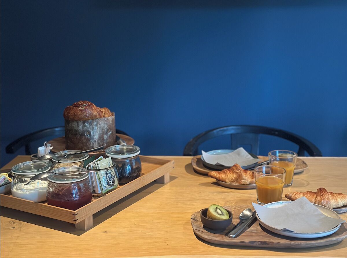 Un plateau de petit-déjeuner comprenant un croissant, un kiwi et une sélection de fromages et de confitures variés.