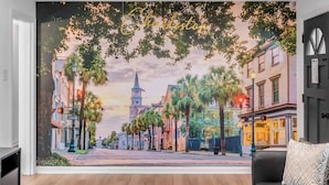 Habitación con un mural de una calle de Charleston, un sofá de cuero negro y una mesita con objetos decorativos.