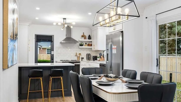 Una cocina moderna con una isla central, taburetes de bar y una mesa de comedor preparada para seis comensales.