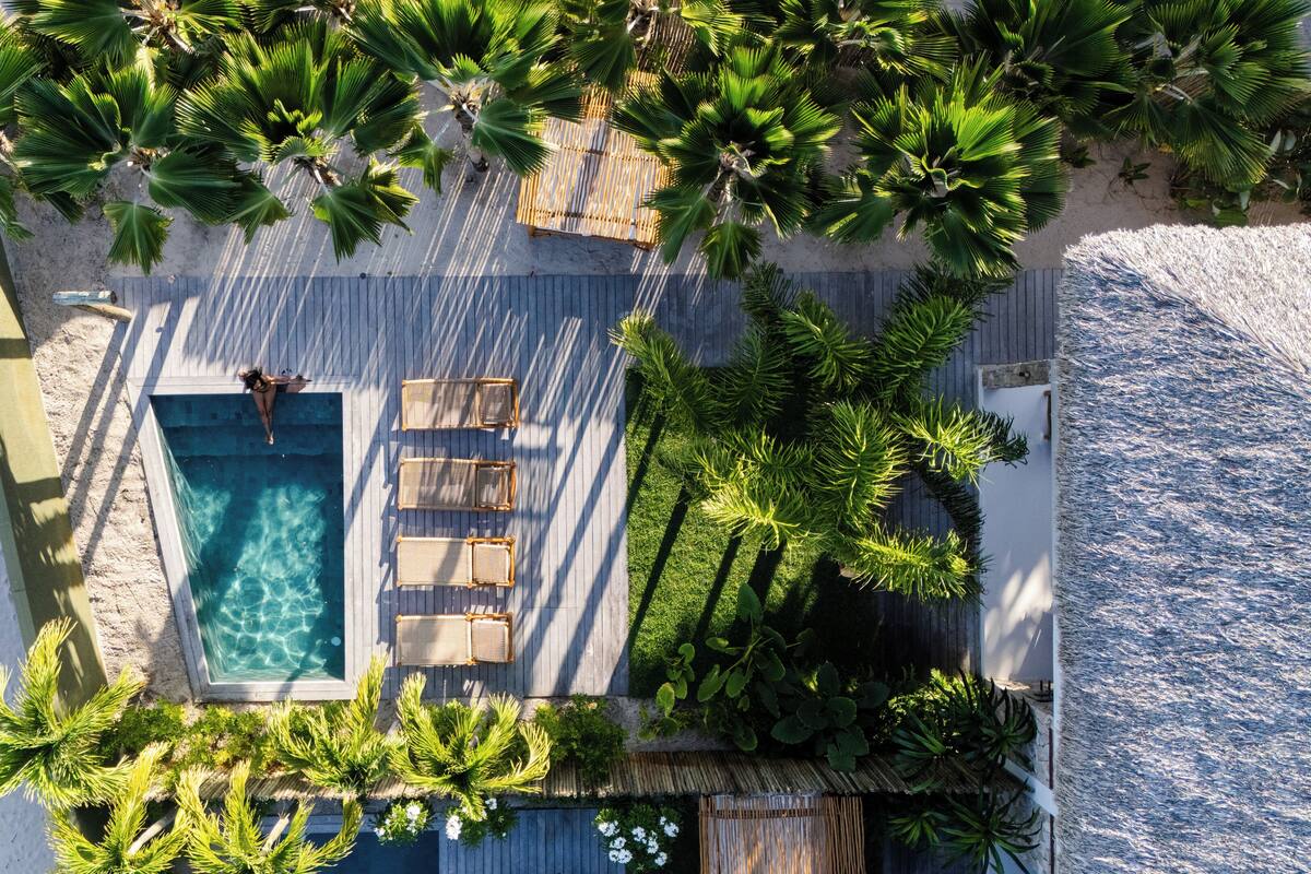 An aerial view of a resort with a swimming pool, lounge chairs, and palm trees.