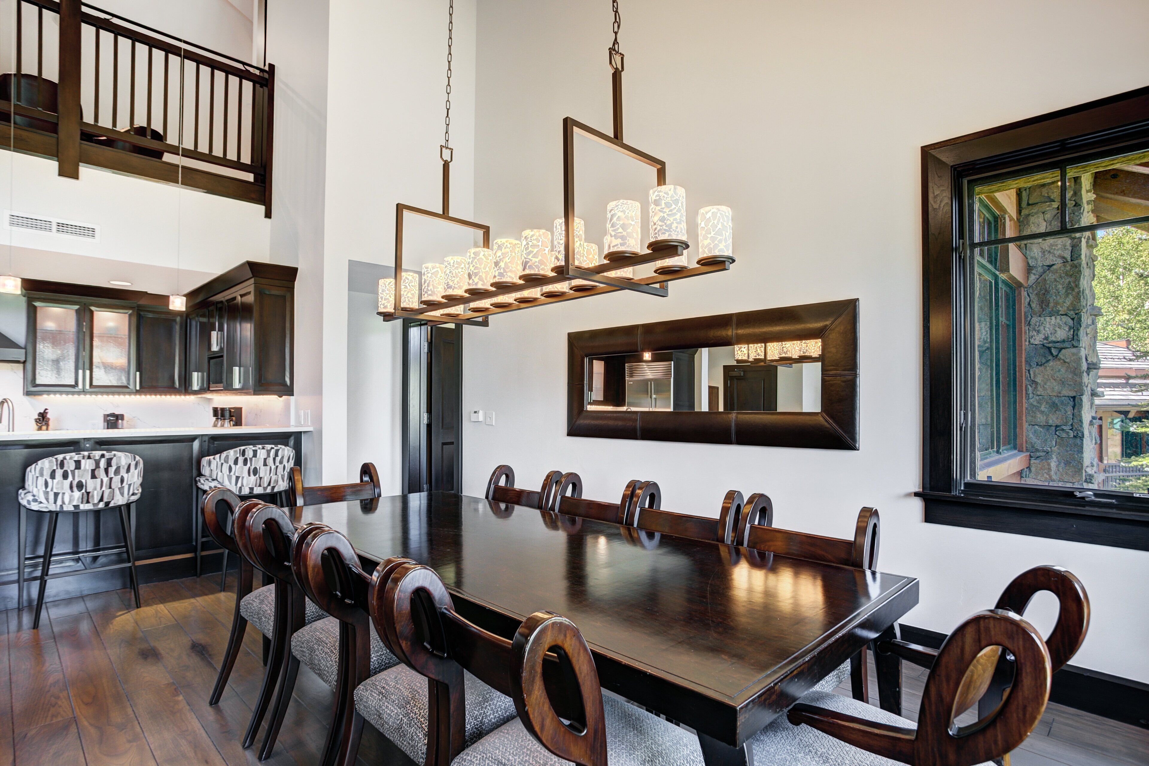 A dining room with a large wooden table, multiple chairs, a chandelier, and a view of the outdoors through a window.