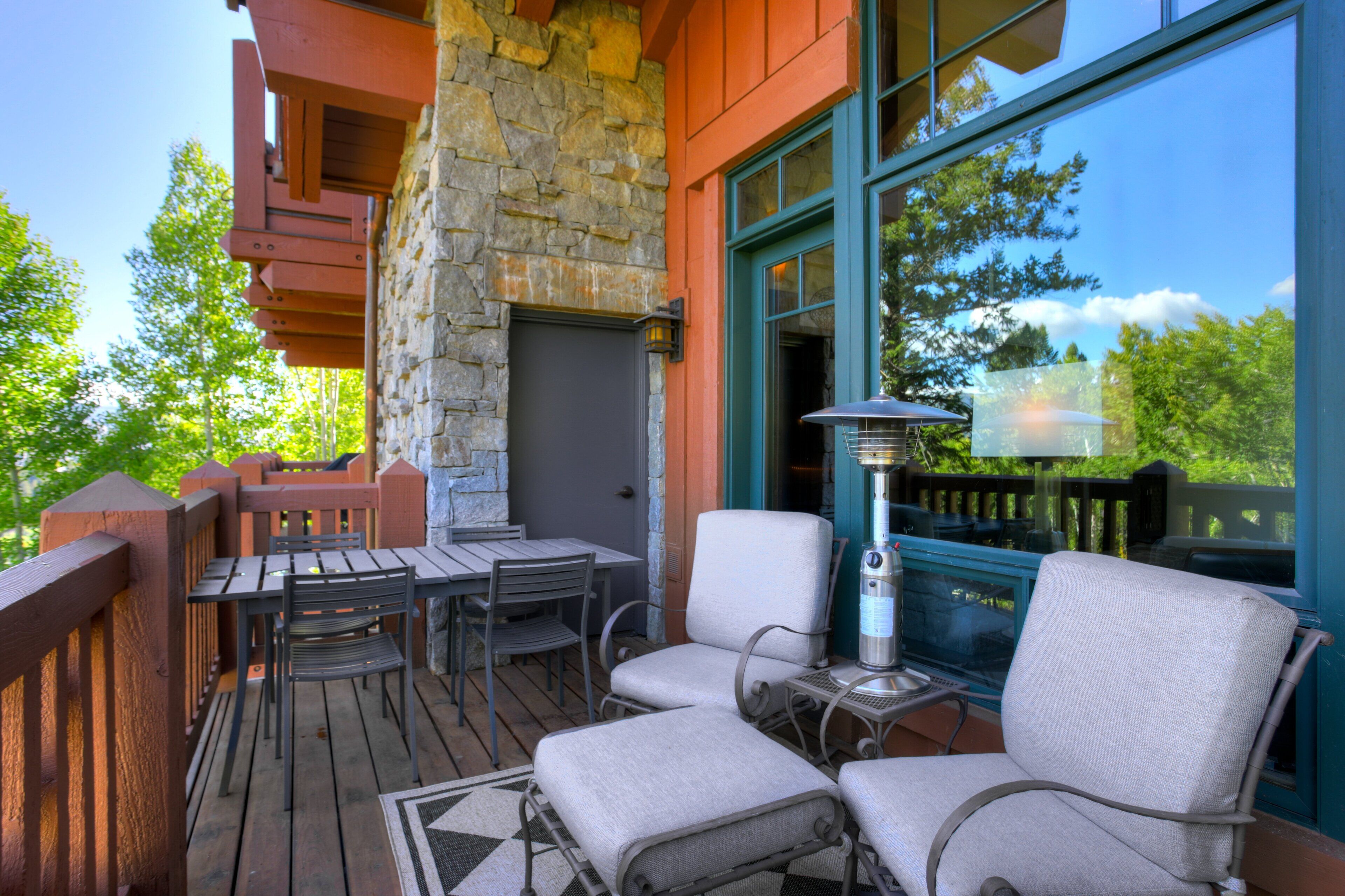 A wooden deck with outdoor furniture, a stone wall, and a large window.