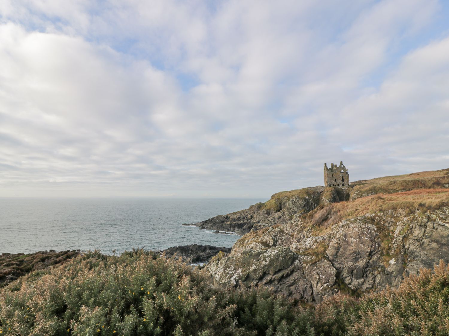 A coastal landscape with a historic stone castle on a cliff overlooking the sea.