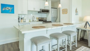 A modern kitchen with white cabinets, a central island with stools, a microwave, oven, and a sink.
