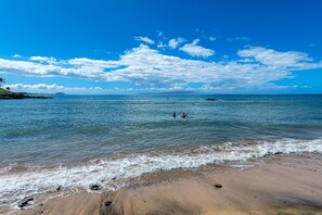 A beach with clear blue water, waves gently lapping onto the shore, and a distant view of a small island.