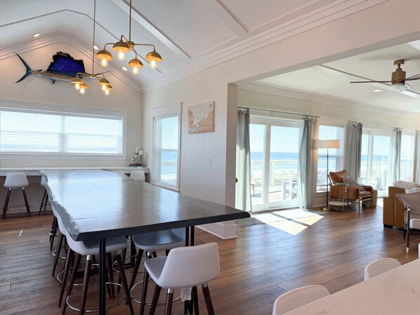 A spacious dining area with a long table, bar stools, and a ceiling fan. - Gulf-Front,Pool, Hot Tub, 5 Kings, Elevator (Saint George Island)
