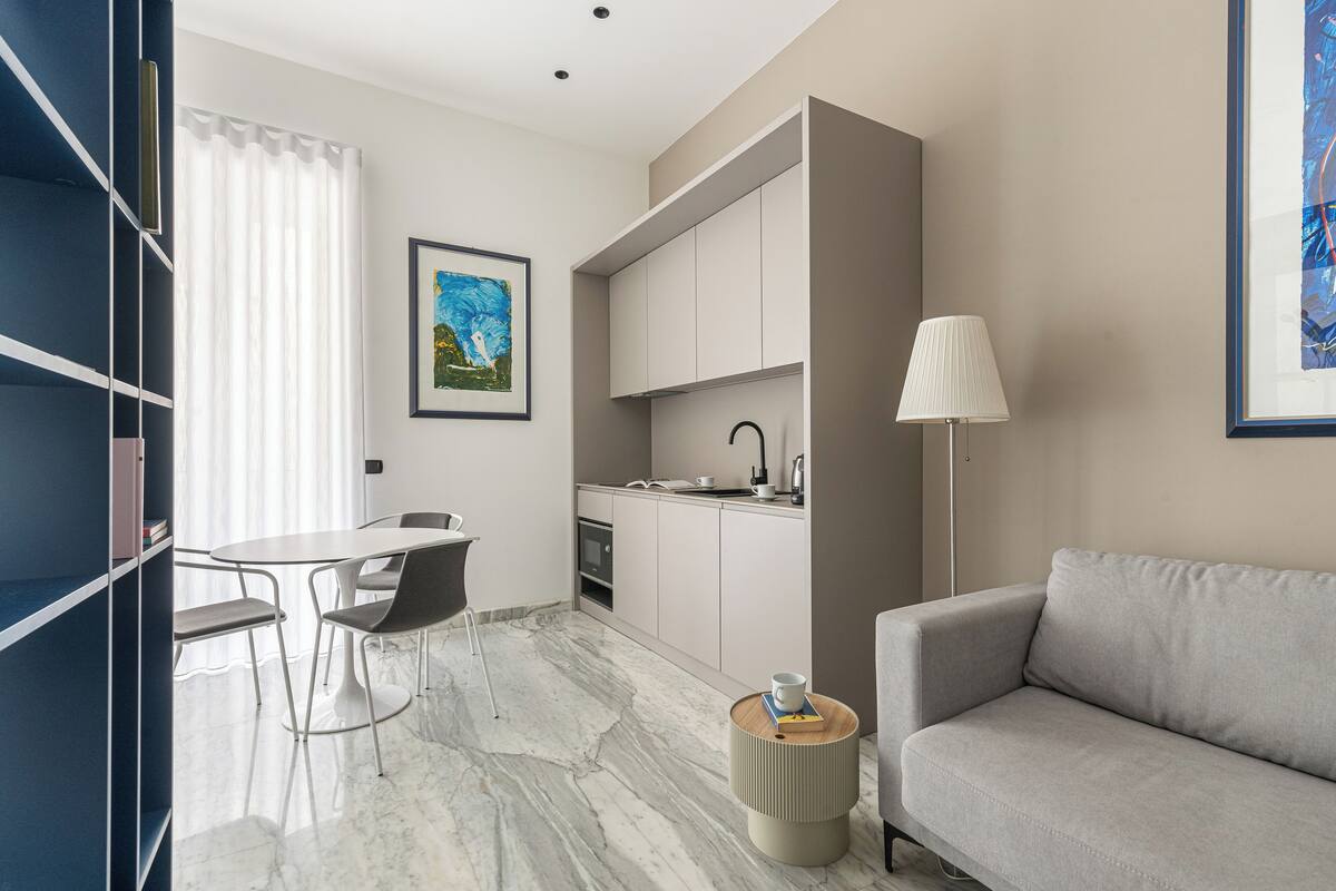 A modern hotel room with a dining area, a sofa, a lamp, and a painting on the wall.