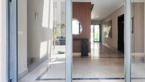 A modern hotel corridor with glass doors, a reception desk, and a view of the outside.