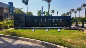 A sign for "Villette New Cairo" with a modern design, palm trees, and a clear sky.