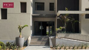 A modern building entrance with a staircase leading to a door, surrounded by potted plants and a metal railing.